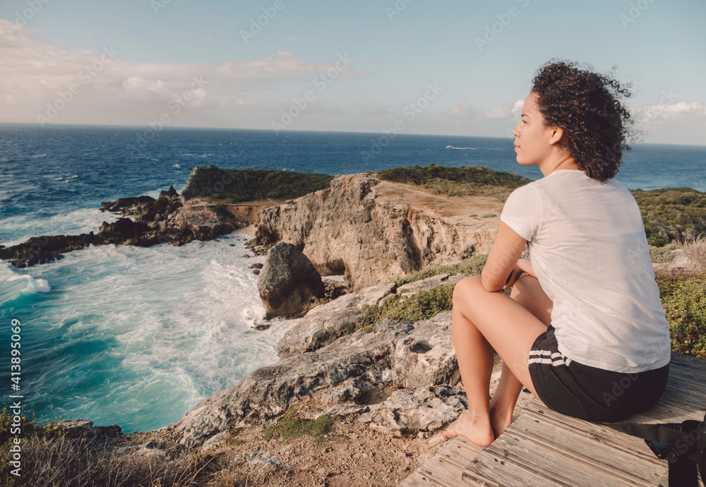 Side view of woman sitting on rock at beach against sky during sunset Side view of woman sitting on rock at beach against sky during sunset