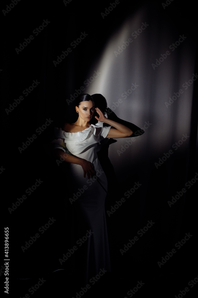 Side profile photo portrait of adorable woman in white dress posing in ray of light on dark studio background Side profile photo portrait of adorable woman in white dress posing in ray of light on dark studio background