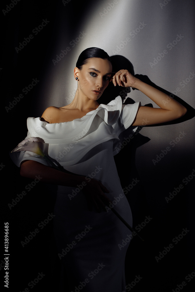 Side profile photo portrait of adorable woman in white dress posing in ray of light on dark studio background Side profile photo portrait of adorable woman in white dress posing in ray of light on dark studio background
