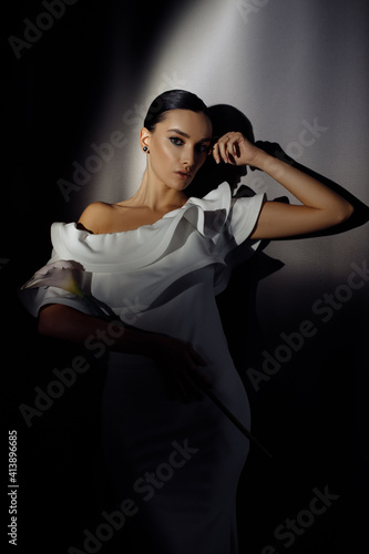 Side profile photo portrait of adorable woman in white dress posing in ray of light on dark studio background