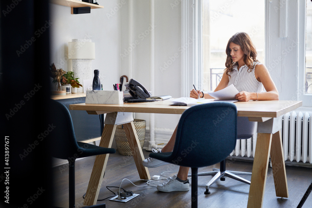 Businesswoman working with documents while sitting at desk in office Businesswoman working with documents while sitting at desk in office