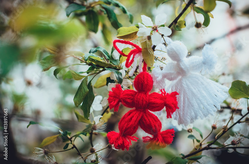 Red and white beautiful martisor hanging on the branches of the blooming tree. Martenitsa beginning of spring celebration. Romania and Bulgaria tradition. White flowers photo