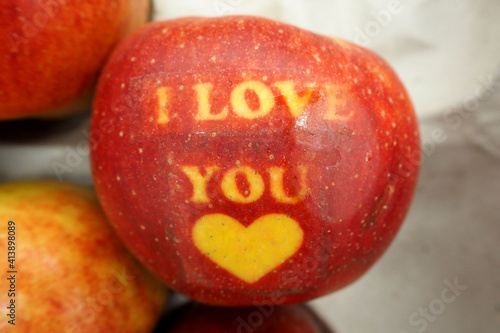 a large red apple with a yellow inscription I love you and a heart lying next to other apples top view