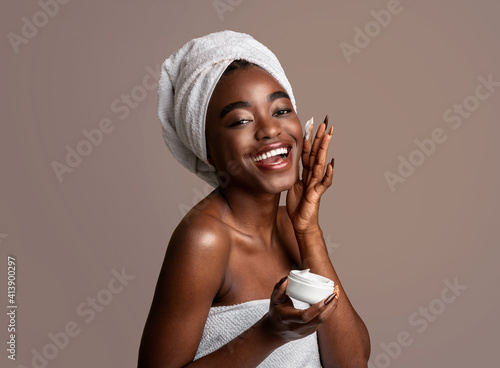 Beautiful young african american woman applying cream on face