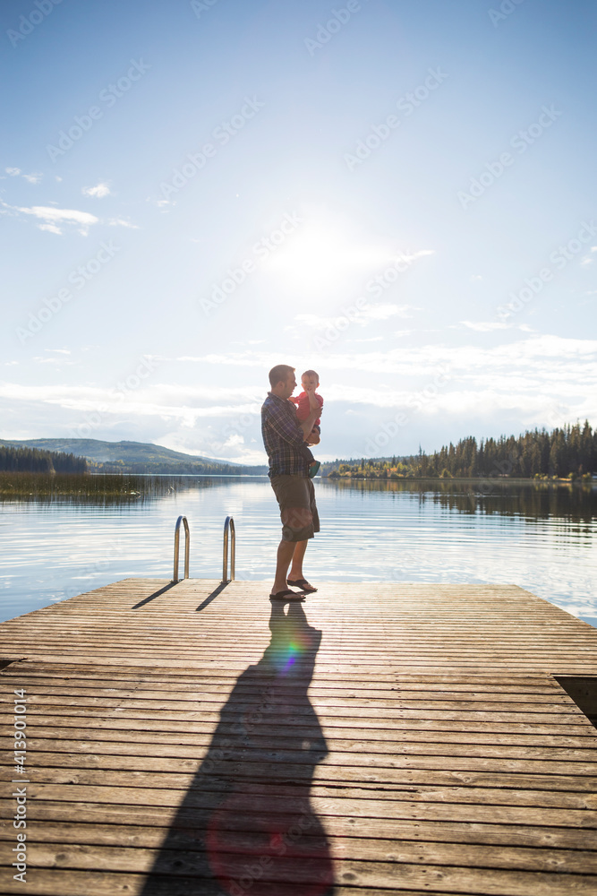 Full length of father carrying son while standing on pier against lake and sky during sunny day Full length of father carrying son while standing on pier against lake and sky during sunny day