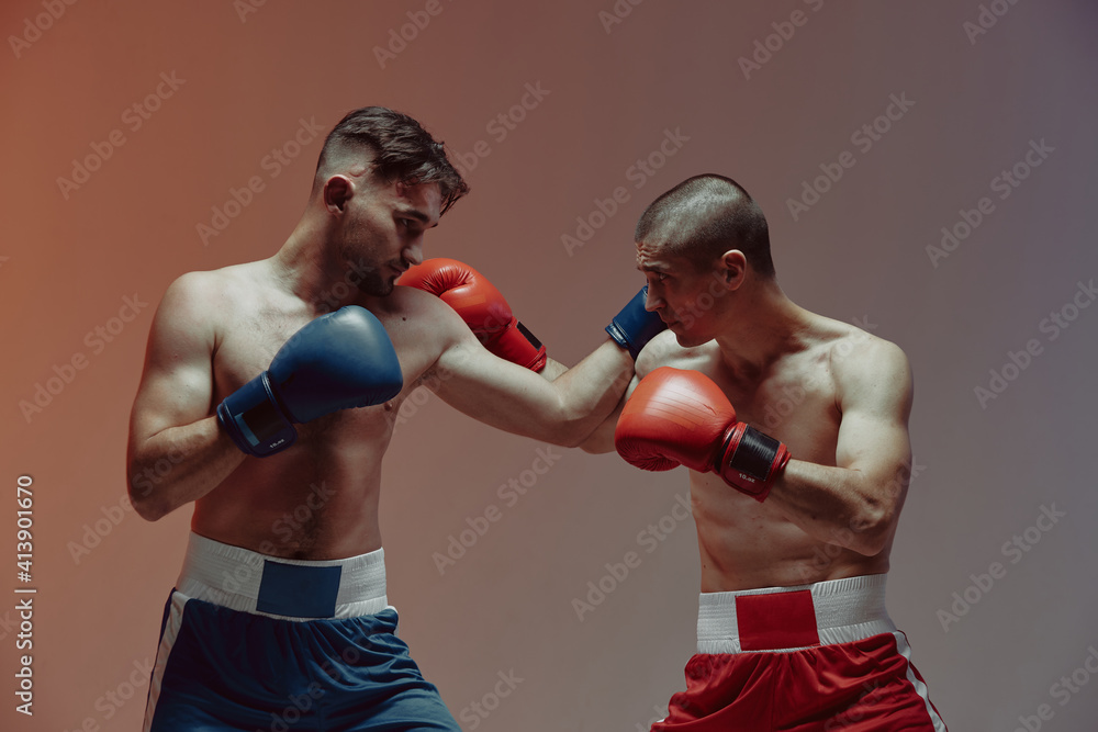 Boxers combat of two fighting males in boxing gloves in red studio light, martial arts, mixed fight concept Boxers combat of two fighting males in boxing gloves in red studio light, martial arts, mixed fight concept