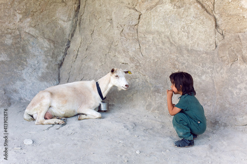 child with a phone is standing on a mountain and goats are walking around