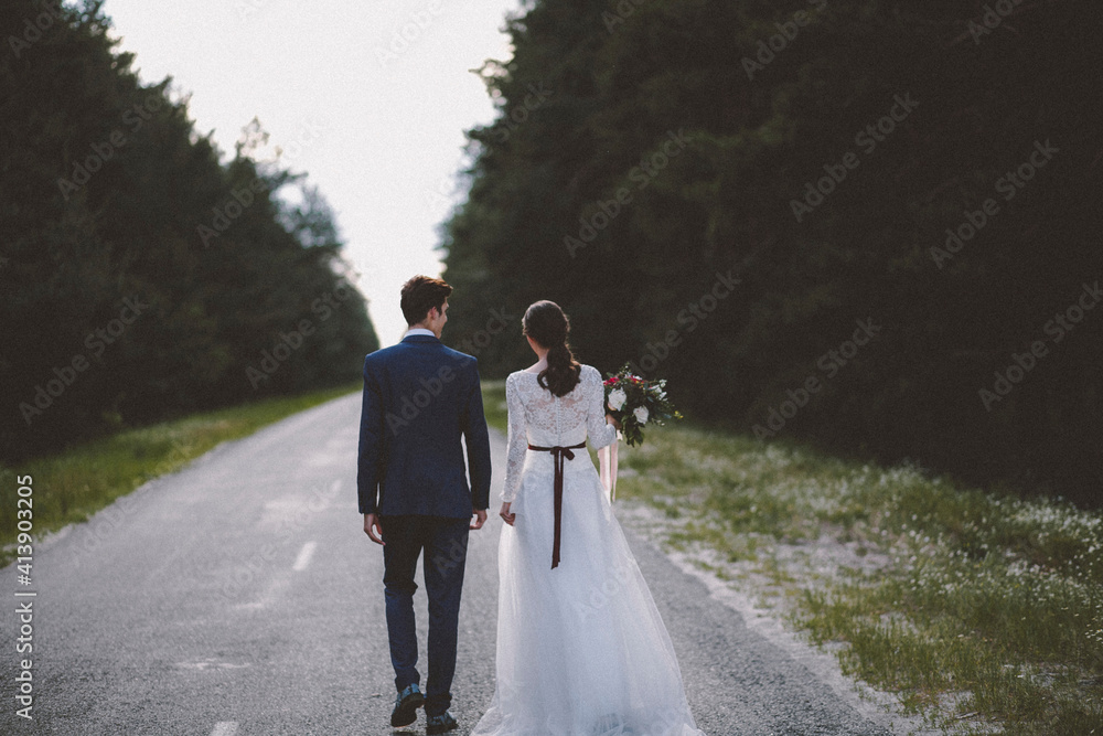 Rear view of bride and groom walking on road amidst trees Rear view of bride and groom walking on road amidst trees