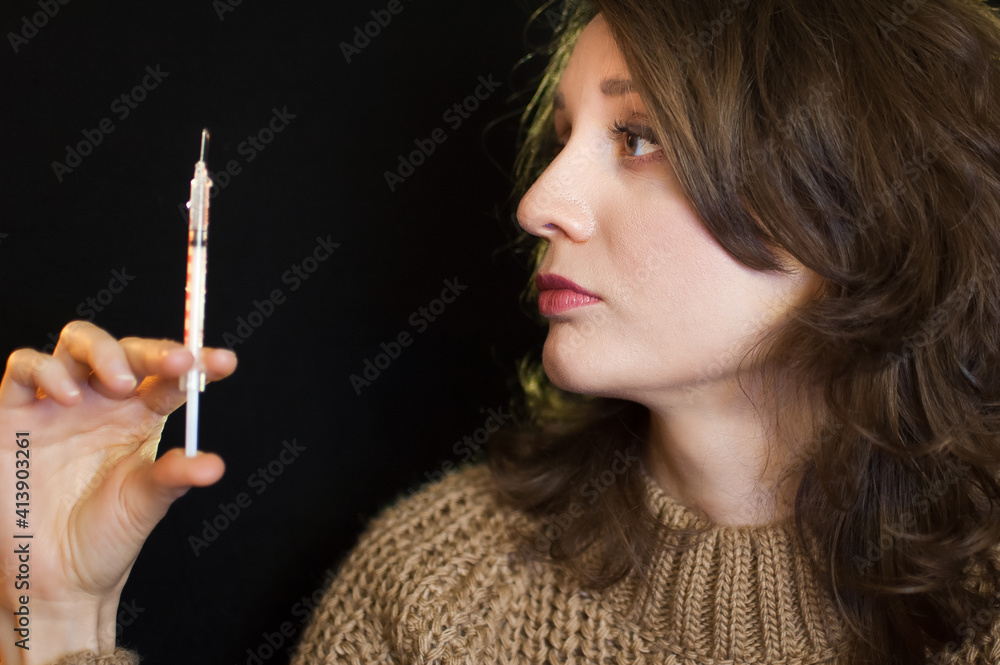 Obraz premium Vaccine concept. Female portrait of caucasian girl holding a syringe and looking at it on black background in studio.