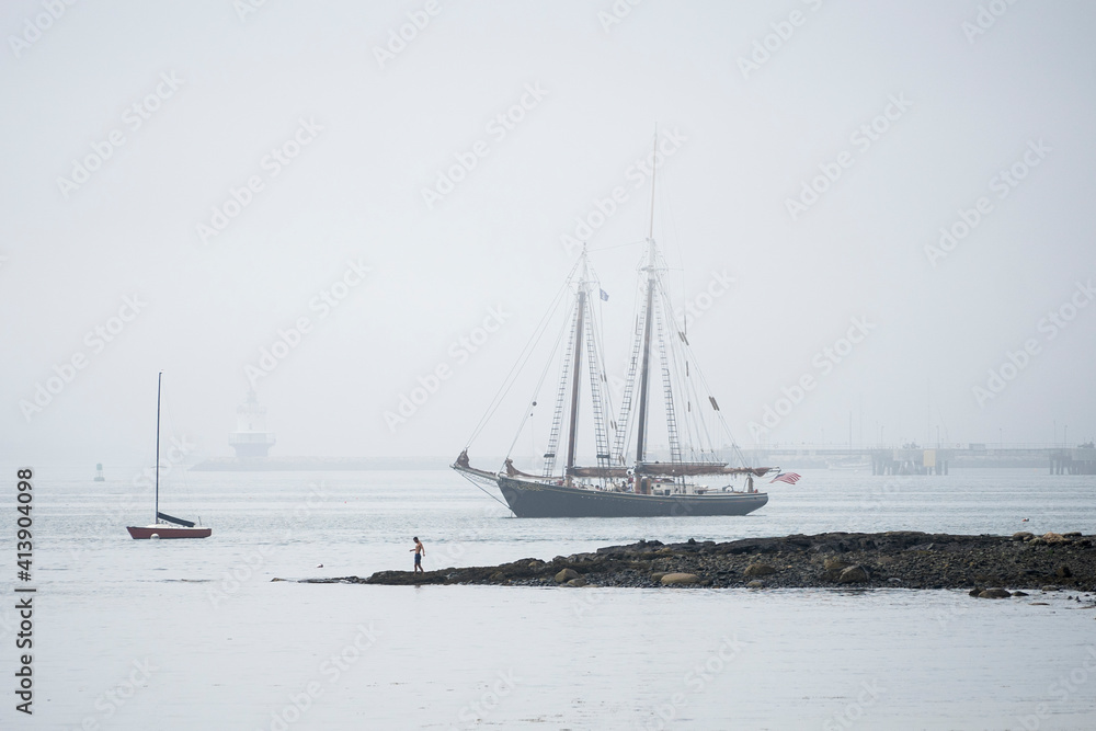 Man exploring shoreline with schooner in the background Man exploring shoreline with schooner in the background