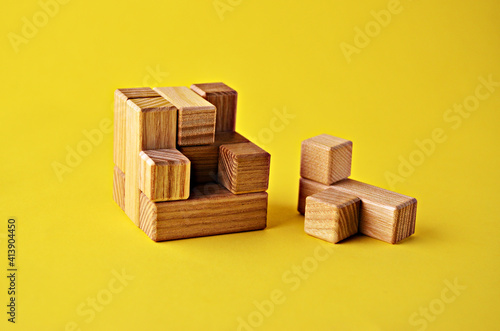 Logical game wooden cube puzzle the last element lies next to the yellow background close up. Solving logical problems. High quality photo