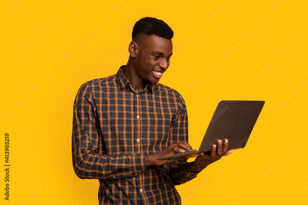 Freelance Work. Portrait Of Smiling African Guy Using Laptop Over Yellow Background Freelance Work. Portrait Of Smiling African Guy Using Laptop Over Yellow Background