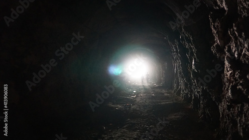 Light at the end of a long cave and children. The sunlight is bright in the eyes while in a long, dark tunnel. Children go to the exit, touching the stone walls. Rock of an artificial mine. © SergeyPanikhin