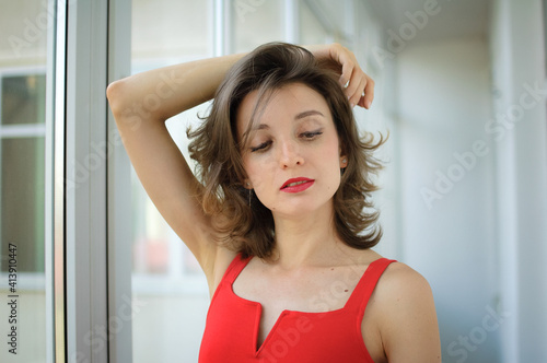 Young attractive woman in red clothes with sensual lips is possing at studio on window background