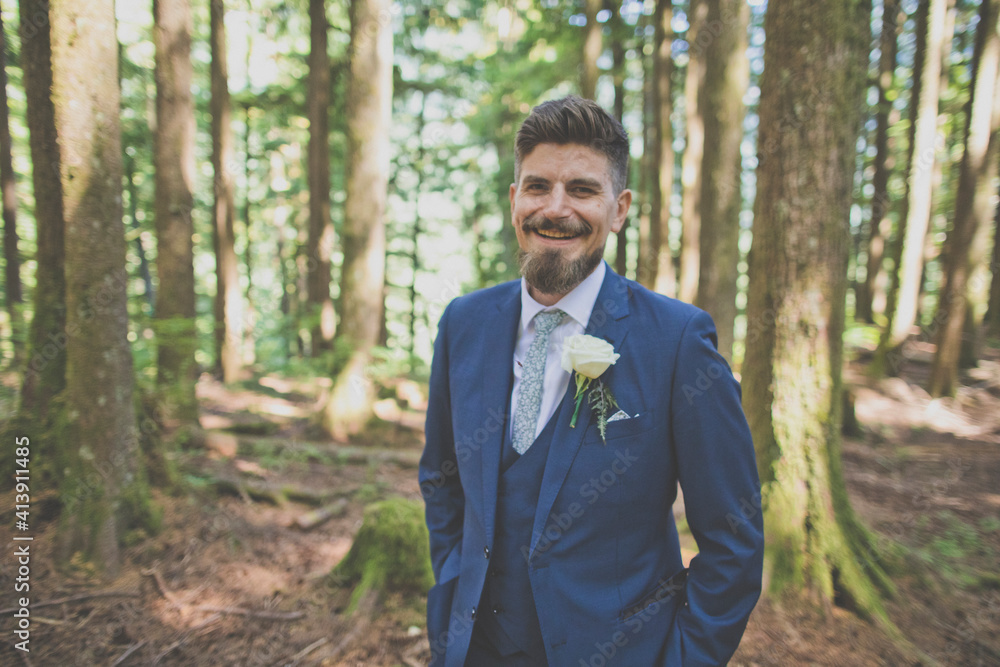 Portrait of happy bridegroom with hands in pockets standing against trees at forest Portrait of happy bridegroom with hands in pockets standing against trees at forest