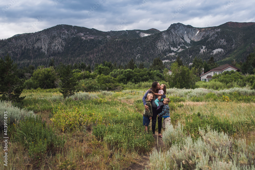 Happy mother with children standing on grassy landscape against cloudy sky in forest Happy mother with children standing on grassy landscape against cloudy sky in forest