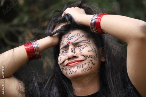 A southeast Asian brown woman protesting gender based violence by writing anti violence against women and girls messages all over her face and looking angry and sad photo