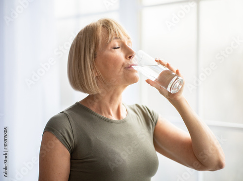 Slika na platnu Fit senior woman drinking clear water during her workout break at home