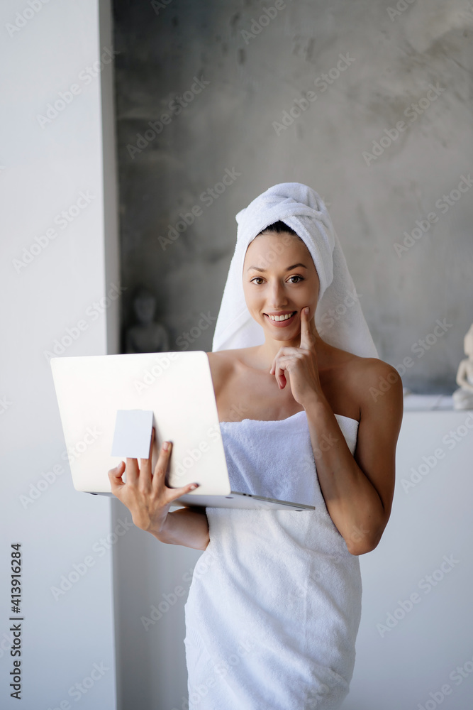 Woman freelancer in white towel stand in the bathroom with a laptop Woman freelancer in white towel stand in the bathroom with a laptop