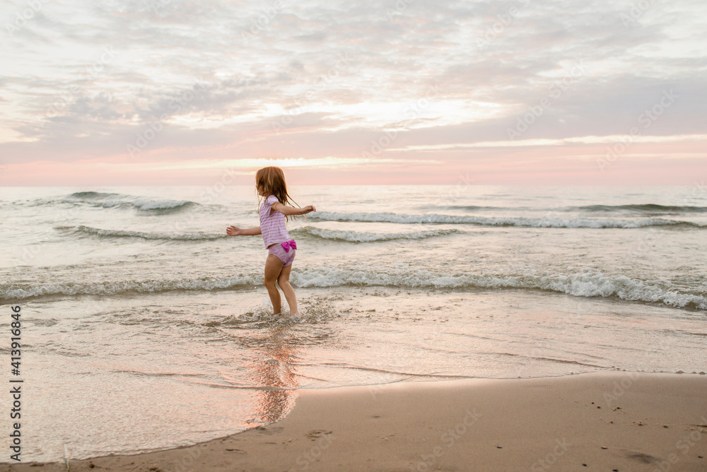 Carefree girl playing on shore at beach against cloudy sky during sunset