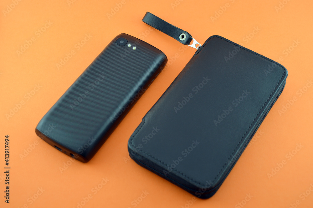 Black leather case and mobile phone on an orange background. Black leather case and mobile phone on an orange background.