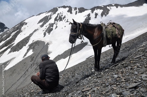 Rider taking rest with his horse near snowy mountain pass photo