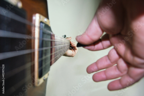 Pessoa a tocar uma guitarra eletroacustica - pormenor da m  o direita com palheta e m  o esquerda focada num acorde - bra  o da guitarra em linha de fuga - guitarra electrica de caixa oca - jazz  blues