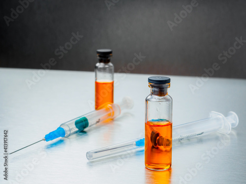 Selective focus. Close-up shot of injection syringes and ampoules with orange coronavirus vaccine on a silver aluminum background. Covid-19 pandemic medical concept. Copy space.