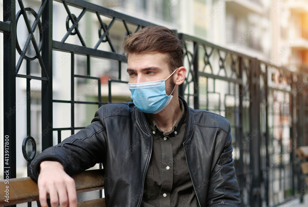 Sad handsome man in medical protective face mask sits on the bench