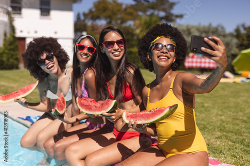 Diverse group of female friends taking selfie with watermelon sitting at the poolside © WavebreakMediaMicro