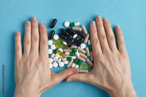 Closeup of white pils and colorful capsules between two hands on a blue background. Heap of pills - medical background photo