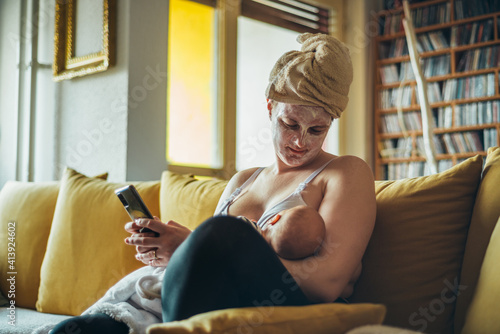 Shot of a busy mom breastfeeding her child while using a smartphone and heaving a beauty treatment while sitting on a couch at home photo