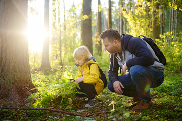School boy and his father hiking together and exploring nature with magnifying glass. Child with his dad spend quality family time together in the sunny summer forest.