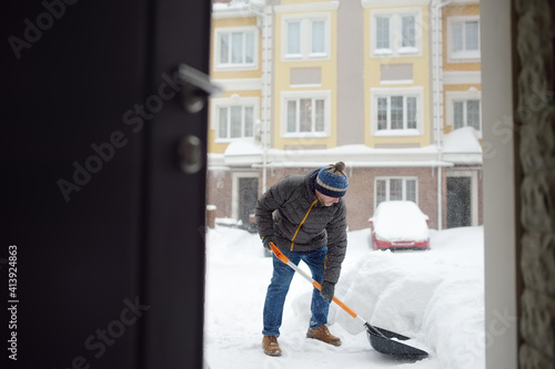 A mature man clean path near house from snow during strong blizzard. Person shoveling snow out of the driveway. Huge snowdrifts. Difficult situation in the city after a snow storm