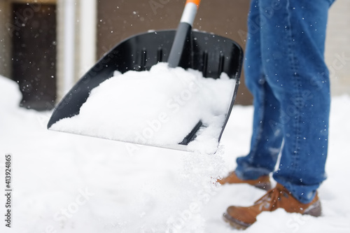 A mature man clean path near house from snow during strong blizzard. Person shoveling snow out of the driveway. Huge snowdrifts. Difficult situation in the city after a snow storm