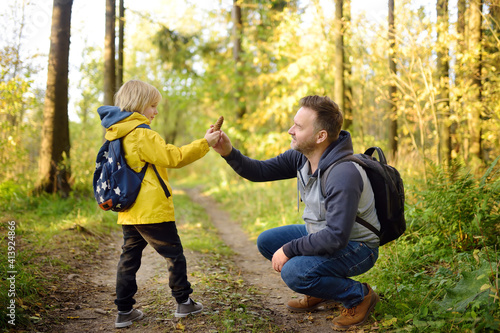 Cute schoolchild and his mature father hiking together and exploring nature. Little boy with his dad spend quality family time together in the sunny summer forest.