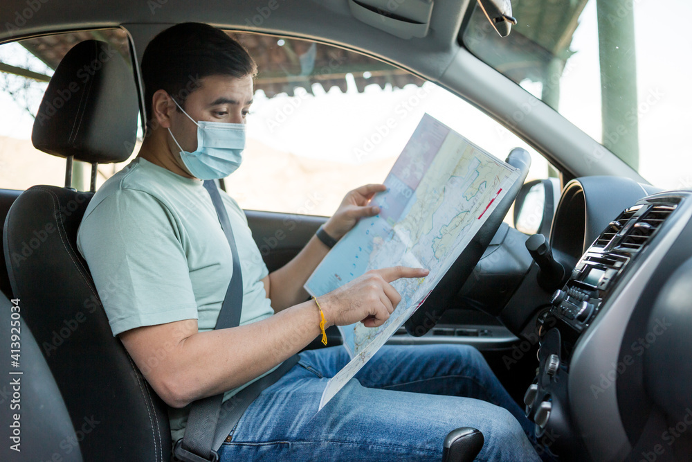Un viajero masculino con una máscara sanitaria sentado en su automóvil mirando mapas