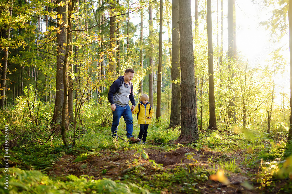 Cute schoolchild and his mature father hiking together and exploring nature. Little boy with his dad spend quality family time together in the sunny summer forest.