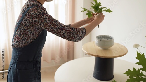 Mujer con mascarilla poniendo un ramo de plantas sobre un jarrón 