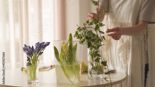 Arreglos de flores con agua sobre la mesa. Mujer sosteniendo unas orquídeas