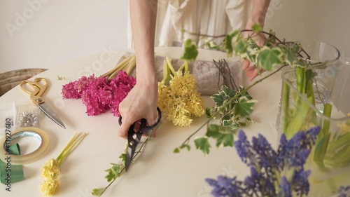 Variedad de flores en la mesa. Mujer agarrando una tijera