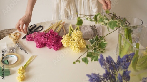 Variedad de flores en la mesa. Mujer ordenando materiales de florería