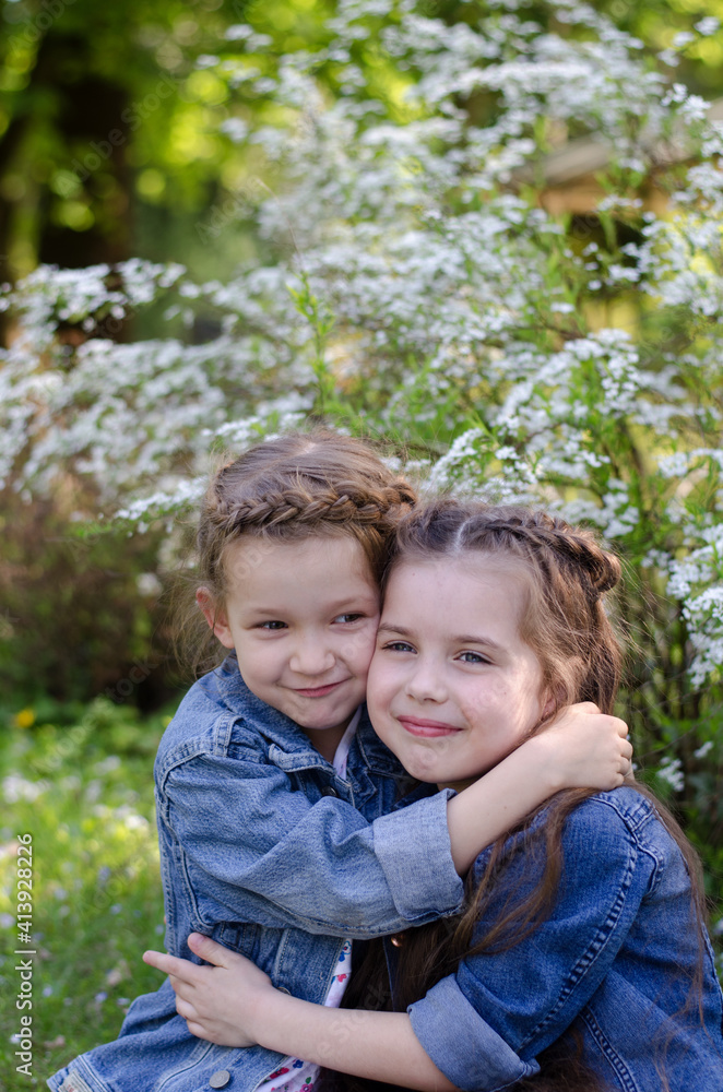 Two adorable little girls hugging each other in the a spring park.