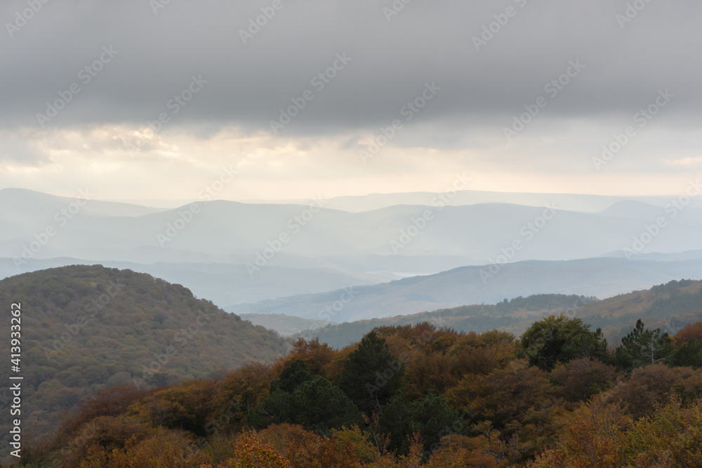 Calm autumn landscape. Beige haze in the mountains. Fantastic light fog at sunset. Atmospheric autumn landscape with mountains and the gold tops of the trees. Background beautiful view with copy space