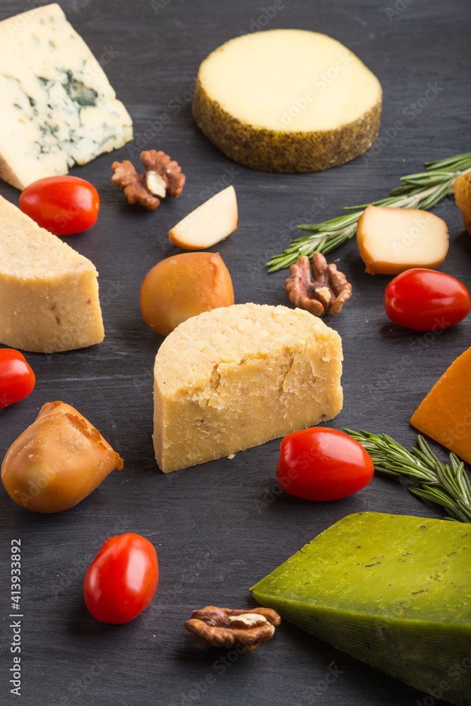 Set of different types of cheese with rosemary and tomatoes on a black wooden background. Side view.