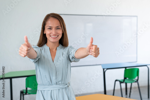 Happy female teacher with thumbs up in classroom. photo