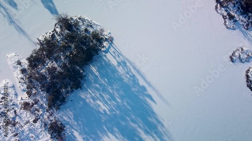 Aerial birdseye view of snowy bog landscape with frozen lakes in sunny winter day, Dunika peat bog (Rucava, Latvia), wide angle drone shot moving left photo