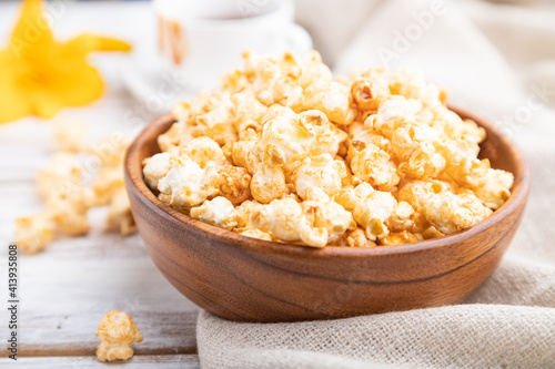 Popcorn with caramel in wooden bowl and a cup of coffee on a white wooden background. Side view, selective focus.