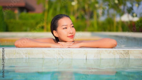 A close up of a pretty young woman with her head resting on her arms along the edge of a swimming pool raises her head and opens her eyes. photo