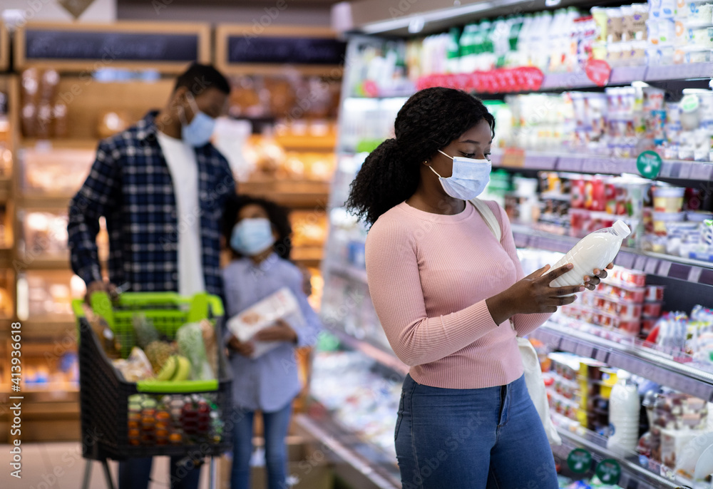 Young black woman with her family purchasing dairy products at modern supermarket during covid quarantine, copy space